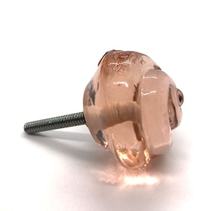 May include: A pink glass cabinet knob with a silver screw. The knob is shaped like a rose.