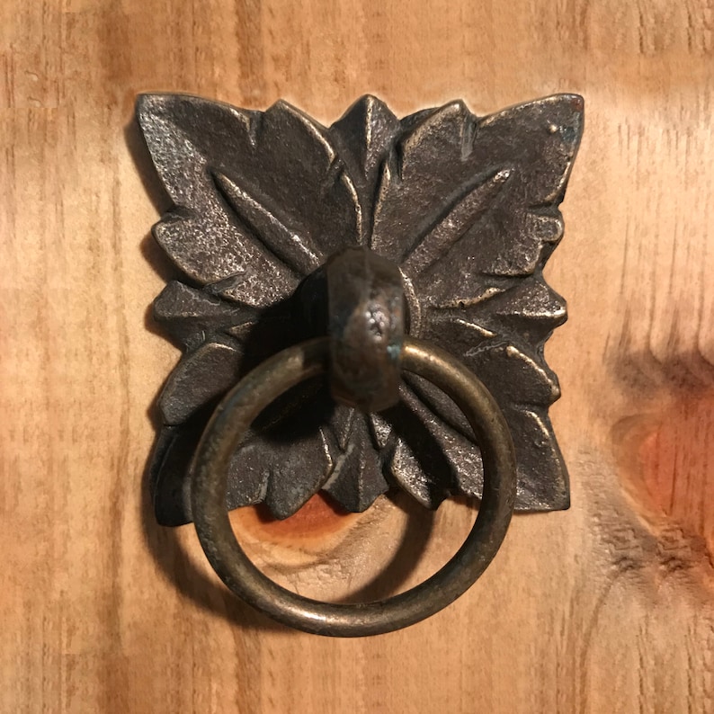May include: A decorative metal ring pull with a detailed floral design. The ring pull is made of a dark metal with a brass finish.
