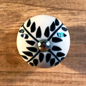 May include: White ceramic knob with a black leaf design and a silver metal center.