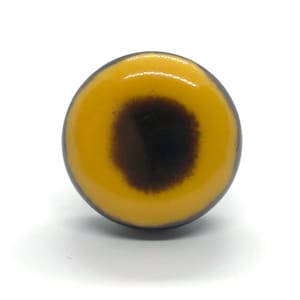 May include: A round, yellow button with a black circle in the center. The button has a glossy finish.