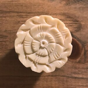 May include: A white carved floral design knob with a raised center. The knob is made of a smooth, ivory-like material.