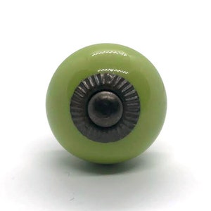 May include: A green ceramic knob with a decorative metal ring around the center. The ring has a raised, textured design.