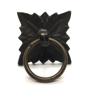 May include: A black metal cabinet pull with a decorative floral design and a ring handle.