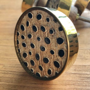 May include: A round, gold-toned cabinet knob with a brown and black patterned design. The pattern features a series of black circles on a brown background.
