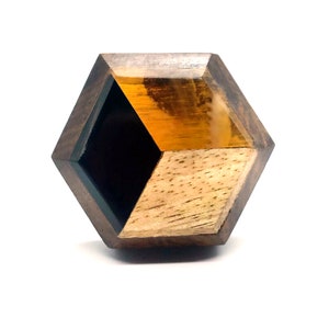May include: A hexagonal wooden ring with a black and amber resin inlay. The ring has a geometric design and is made of dark wood.