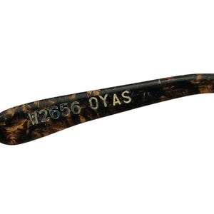May include: Close-up of the inside of a tortoiseshell-patterned glasses frame with the text "W2656 OYAS" printed in white.