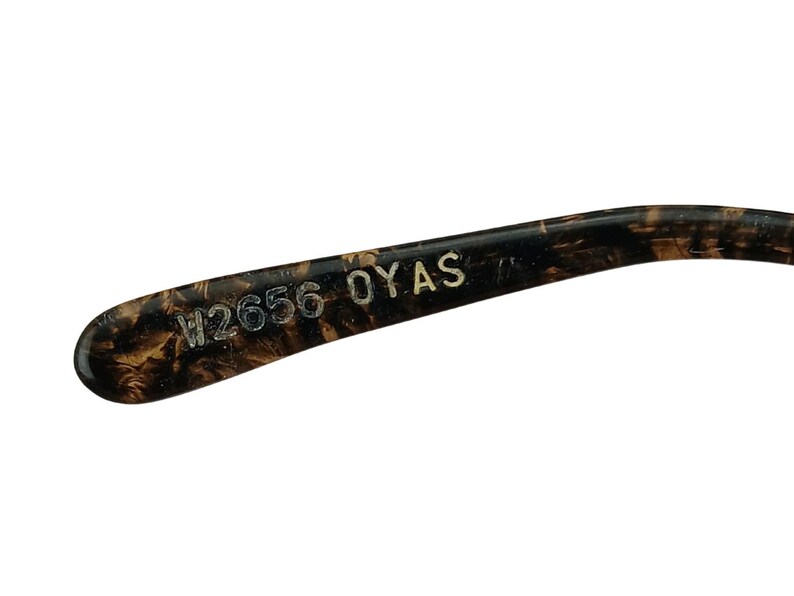 May include: Close-up of the inside of a tortoiseshell-patterned glasses frame with the text "W2656 OYAS" printed in white.