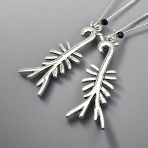 May include: A pair of silver-toned earrings with a unique, stylized design. Each earring features a curved top and a central stem with multiple, outward-pointing branches. Small black beads accent the top of each earring.