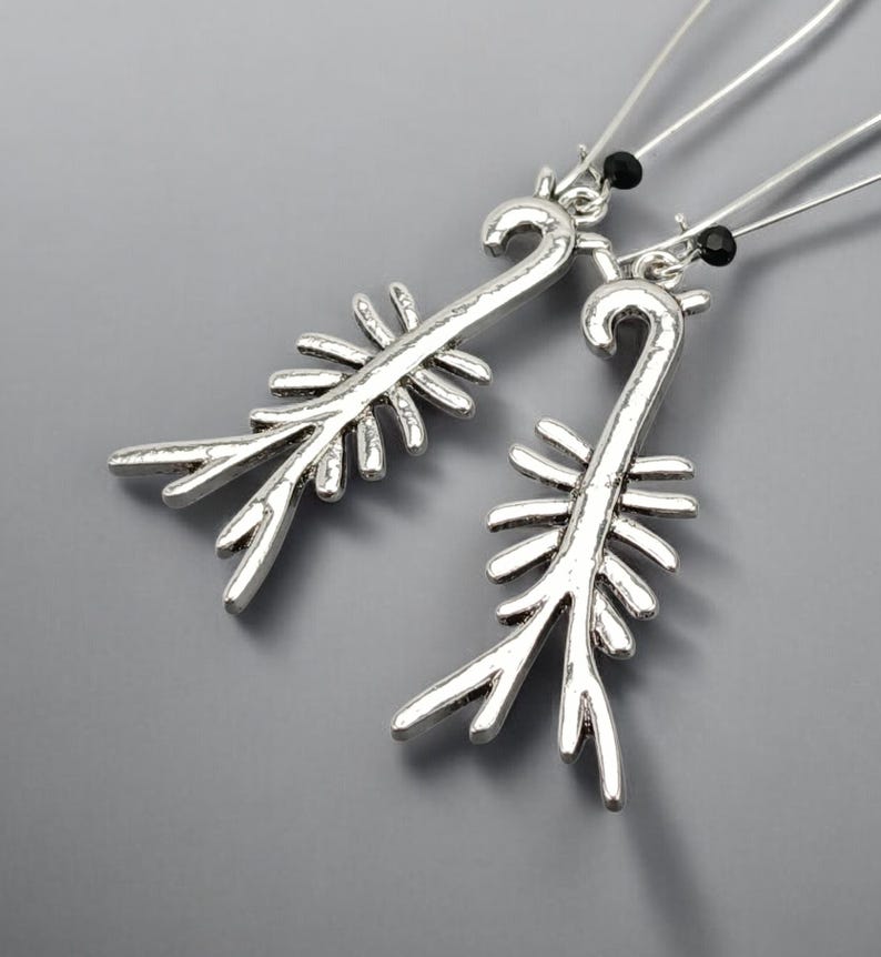 May include: A pair of silver-toned earrings with a unique, stylized design. Each earring features a curved top and a central stem with multiple, outward-pointing branches. Small black beads accent the top of each earring.