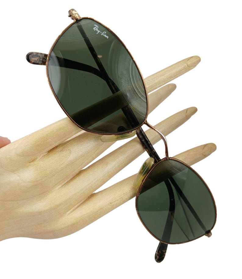 May include: Vintage Ray-Ban sunglasses with a gold metal frame and green lenses. The sunglasses have a rounded, oval shape.