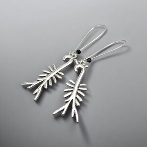 May include: A pair of silver-toned earrings with a unique, stylized design. Each earring features a long, curved hook and a decorative element resembling a stylized plant or feather. Small black beads accent the top of each earring.