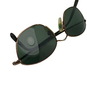 May include: A pair of vintage gold-tone sunglasses with green lenses. The lenses have a circular pattern reflected in them.