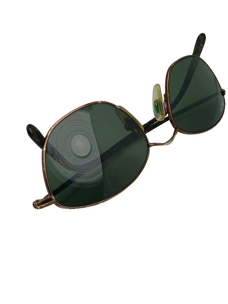 May include: A pair of vintage gold-tone sunglasses with green lenses. The lenses have a circular pattern reflected in them.