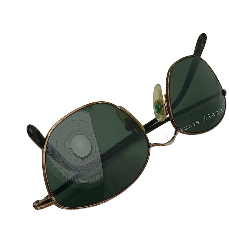 May include: A pair of vintage aviator sunglasses with a gold metal frame and green lenses. The lenses have a circular pattern of scratches.