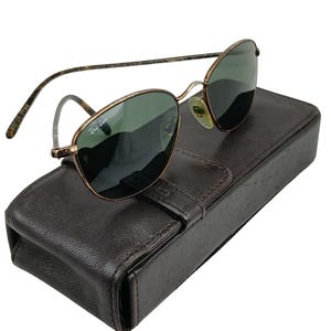 May include: Gold-tone Ray-Ban sunglasses with green lenses and a brown leather case.