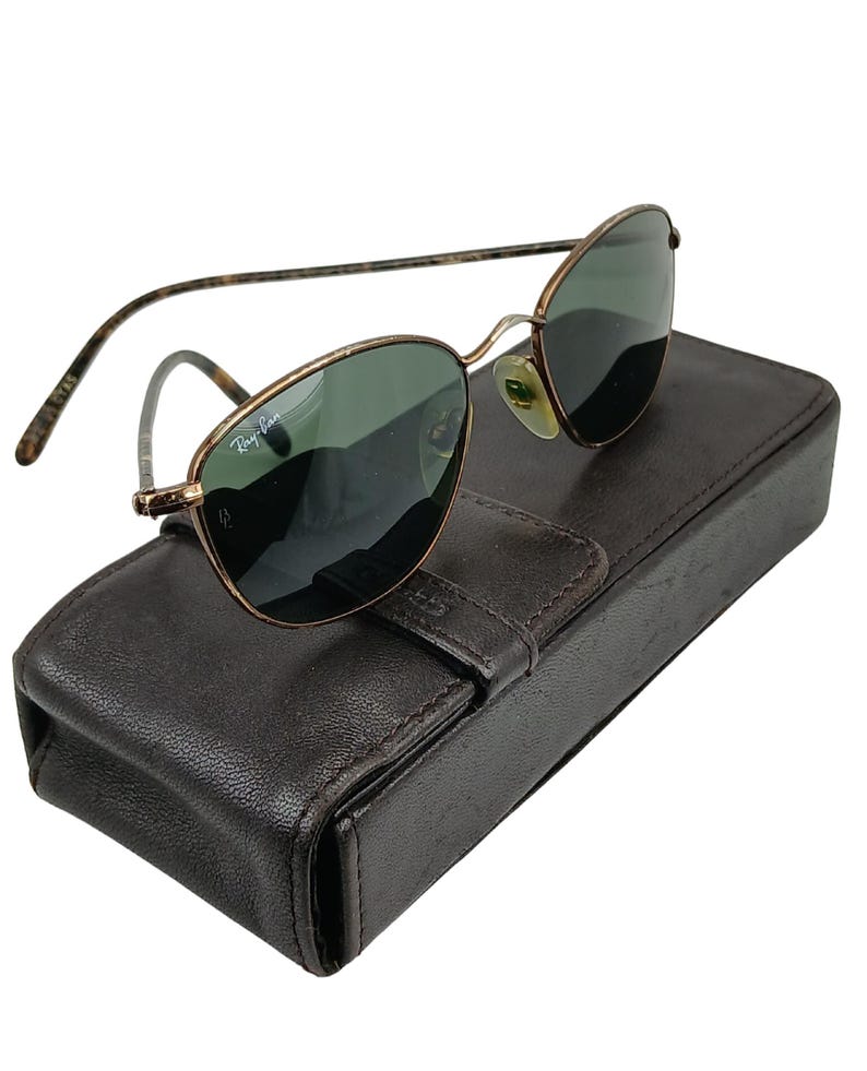 May include: Gold-tone Ray-Ban sunglasses with green lenses and a brown leather case.