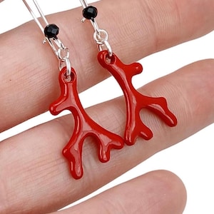 May include: A pair of red coral earrings with silver hooks and black beads. The coral is shaped like a branch with multiple offshoots.