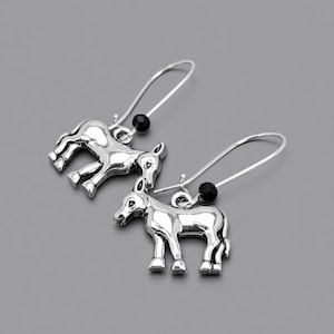 May include: A pair of silver-toned donkey earrings. Each earring features a small, detailed donkey charm suspended from a curved ear wire. A small black bead accents each earring. The earrings are displayed against a gray background.