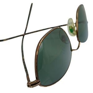 May include: A pair of gold-toned aviator sunglasses with green lenses. The sunglasses have a classic design with a thin metal frame and a rounded shape.