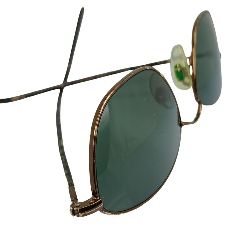 May include: A pair of gold-toned aviator sunglasses with green lenses. The sunglasses have a classic design with a thin metal frame and a rounded shape.