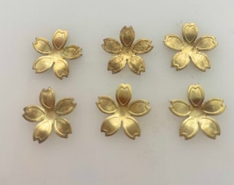 Puede incluir: Seis abalorios de metal dorado en forma de flor con cinco pétalos cada uno. Los abalorios son todos del mismo tamaño y forma.