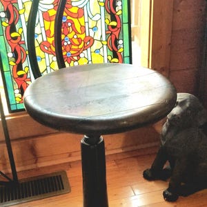 May include: A black swivel stool with a wooden seat and a star-shaped base. The stool is in front of a stained glass window with colorful designs.