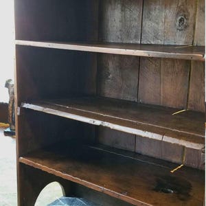 May include: A wooden bookcase with three shelves. The bookcase is dark brown and has a rustic appearance. It is standing on a gray and white patterned rug.