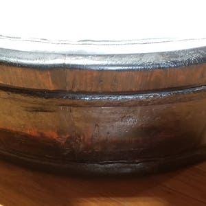 May include: A large, round wooden tub with a dark brown stain. The tub has a wide rim and is made of thick wood planks.