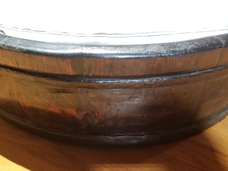 May include: A large, round wooden tub with a dark brown stain. The tub has a wide rim and is made of thick wood planks.