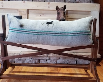 Puede incluir: Una manta de silla de montar de caballo a rayas grises y blancas con una silueta de caballo negro bordada en ella. La manta está en un soporte de silla de montar de madera con una figura de cabeza de caballo marrón en la parte superior.