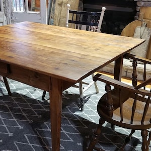 May include: A rustic wooden table with a single drawer and a distressed finish. The table is set with two wooden chairs, one with a woven seat and the other with a solid wood seat.