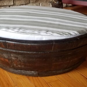 May include: A round, wooden pet bed with a gray and white striped cushion. The bed is made of dark wood and has a slightly distressed finish.