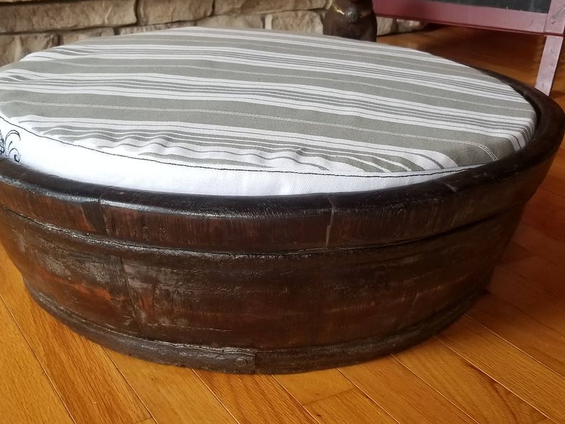 May include: A round, wooden pet bed with a gray and white striped cushion. The bed is made of dark wood and has a slightly distressed finish.