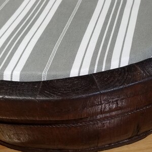 May include: A round, dark brown wooden ottoman with a gray and white striped fabric top.