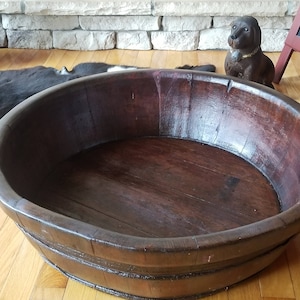 May include: A large, dark brown wooden bowl with a wide, rounded base and a smooth, polished interior. The bowl is made of thick, sturdy wood and has a natural, rustic look.