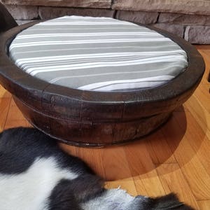 May include: A dark brown wooden pet bed with a white and gray striped cushion. The bed is round and has a wide rim.