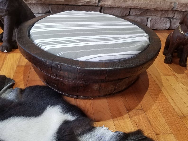 May include: A dark brown wooden pet bed with a white and gray striped cushion. The bed is round and has a wide rim.