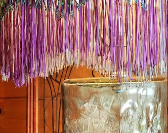 May include: A purple lampshade with a beaded fringe and a clear glass base. The lampshade has a silver trim and the base has a textured surface.