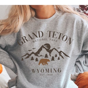 May include: Gray sweatshirt with a brown graphic design of mountains, a bear, and the text "Grand Teton National Park Wyoming Est. 1929."