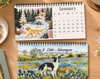 May include: A 2027 desk calendar titled Dogs & Little Adventures featuring a black and white dog in a field of blue flowers on the cover and a golden retriever in a snowy landscape with a January calendar grid on the open page above.