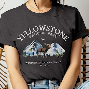 May include: A dark gray heather t-shirt with a white graphic print of Yellowstone National Park. The graphic includes a moose, mountains, trees, and the text 'Yellowstone National Park' and 'Wyoming, Montana, Idaho Est. 1872'.