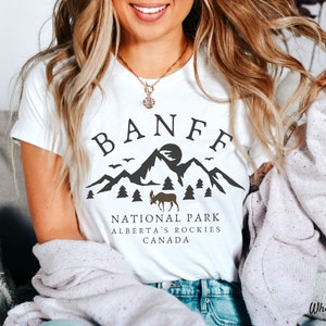 May include: White t-shirt with a black graphic design that says "Banff National Park, Alberta's Rockies, Canada". The graphic includes a mountain range, a moose, and trees.