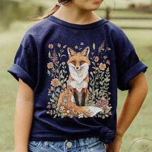 May include: Navy blue t-shirt featuring a detailed illustration of a fox surrounded by flowers. The fox has orange and white fur, and the flowers are in shades of orange, pink, and purple. The shirt is paired with denim shorts.