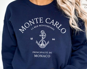 Könnte beinhalten: Ein marineblaues Sweatshirt mit Rundhalsausschnitt und weißem Aufdruck, der MONTE CARLO, LA MER MÉDITERRANÉE, 1866 und PRINCIPAUTÉ DE MONACO liest, zentriert um eine detaillierte weiße Grafik eines mit einem Seil umwickelten Schiffsankers.