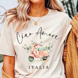 May include: A white t-shirt with a watercolor illustration of a pink scooter with green leaves and the text "Ciao Amore ITALIA".