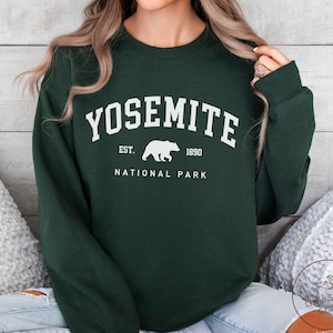 Op de afbeelding: Een donker bosgroene sweater met ronde hals en witte opdruk met de tekst YOSEMITE NATIONAL PARK, EST. 1890 en een silhouet van een beer in het midden. De trui met lange mouwen heeft een geribbelde halslijn en een effen ontwerp.