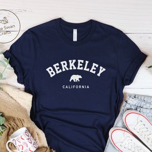 May include: Navy blue t-shirt with white text that reads "Berkeley, California" and a white silhouette of a bear.