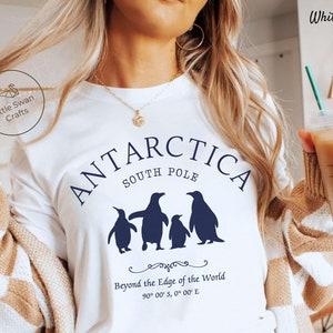 May include: White t-shirt with a blue graphic of penguins and the text "ANTARCTICA SOUTH POLE" and "Beyond the Edge of the World 90° 00' S, 0° 00' E".