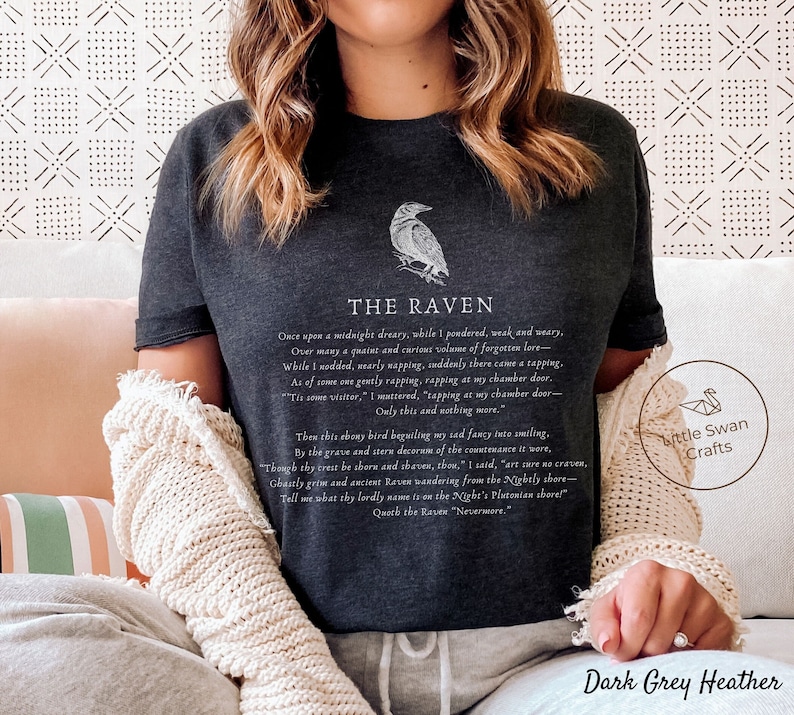 Puede incluir: Camiseta de color gris oscuro jaspeado con una ilustraci&oacute;n de un cuervo negro y el texto "The Raven" con un extracto del poema "The Raven" de Edgar Allan Poe.