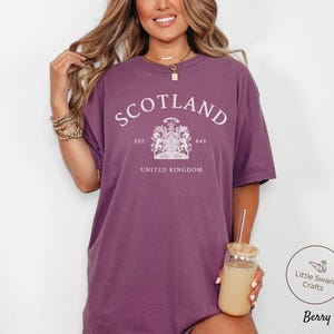 Pode incluir: Uma camiseta cor de baga com a palavra "SCOTLAND" em arco no peito. Abaixo, um bras&atilde;o e as palavras "EST. 843" e "UNITED KINGDOM". A camiseta tem um corte folgado.